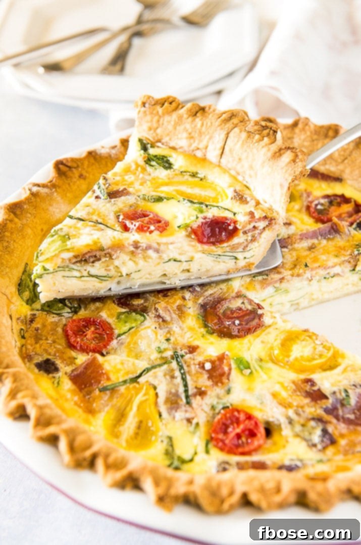 A perfectly baked slice of Bacon Onion Spinach Quiche Lorraine on a pie server, showcasing its golden crust and rich filling.