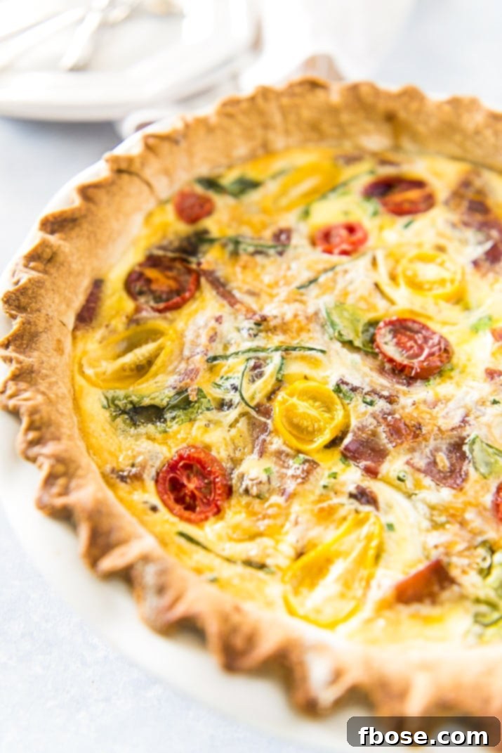 A whole, beautifully baked Bacon Onion Spinach Quiche Lorraine in a pie dish, ready to be served.