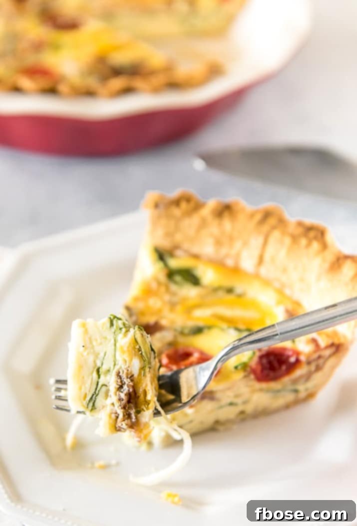 A fork taking a bite from a delicious slice of Bacon Onion Spinach Quiche Lorraine.