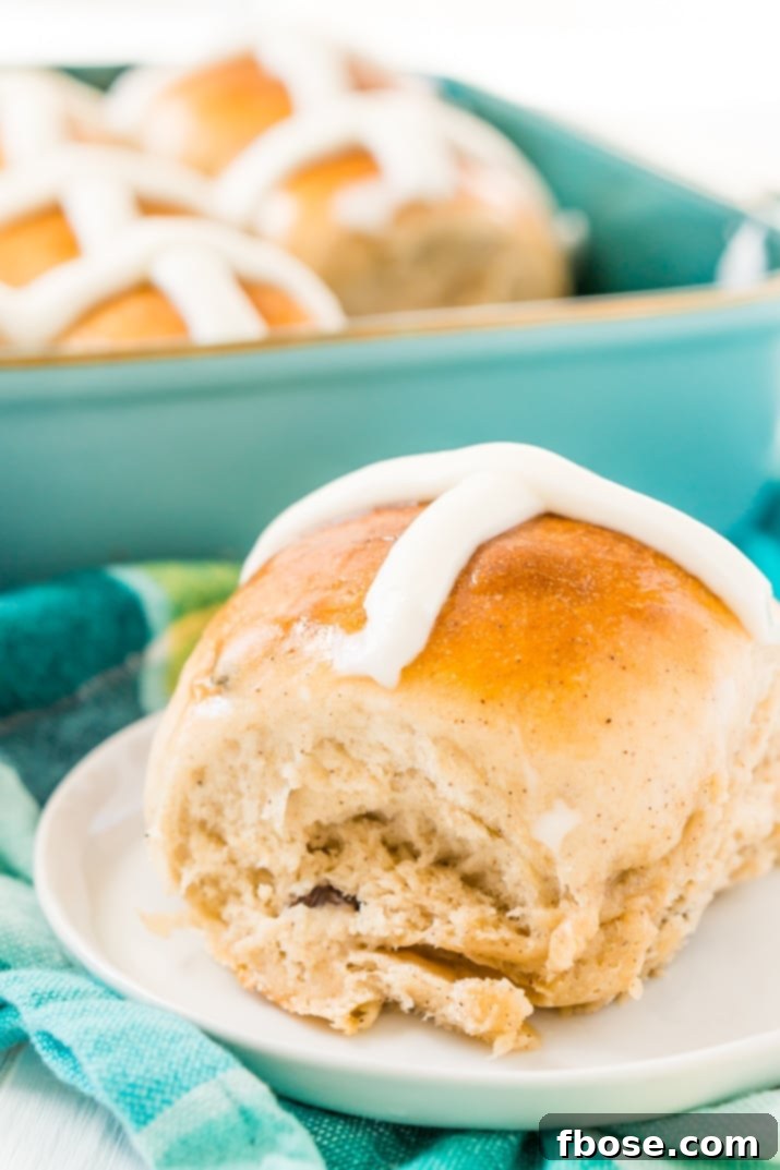 A perfectly baked hot cross bun on a white plate with a blue linen napkin, ready to be enjoyed.