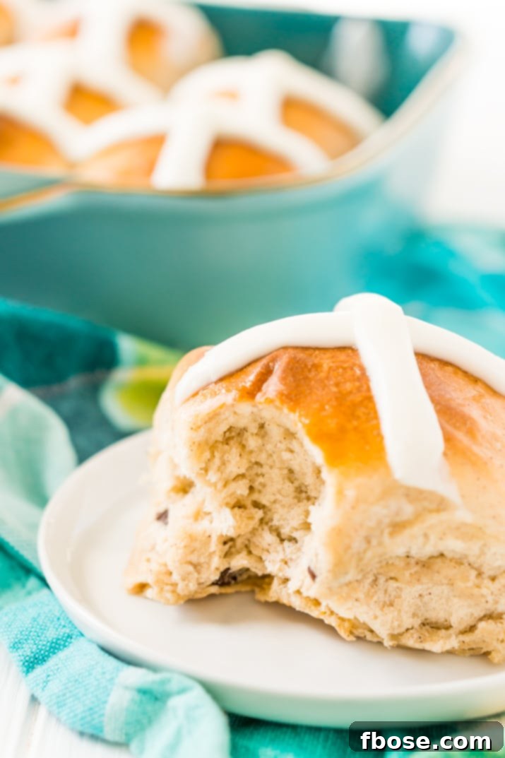 A hot cross bun with a bite taken out, revealing its soft, fluffy interior and fruity filling.