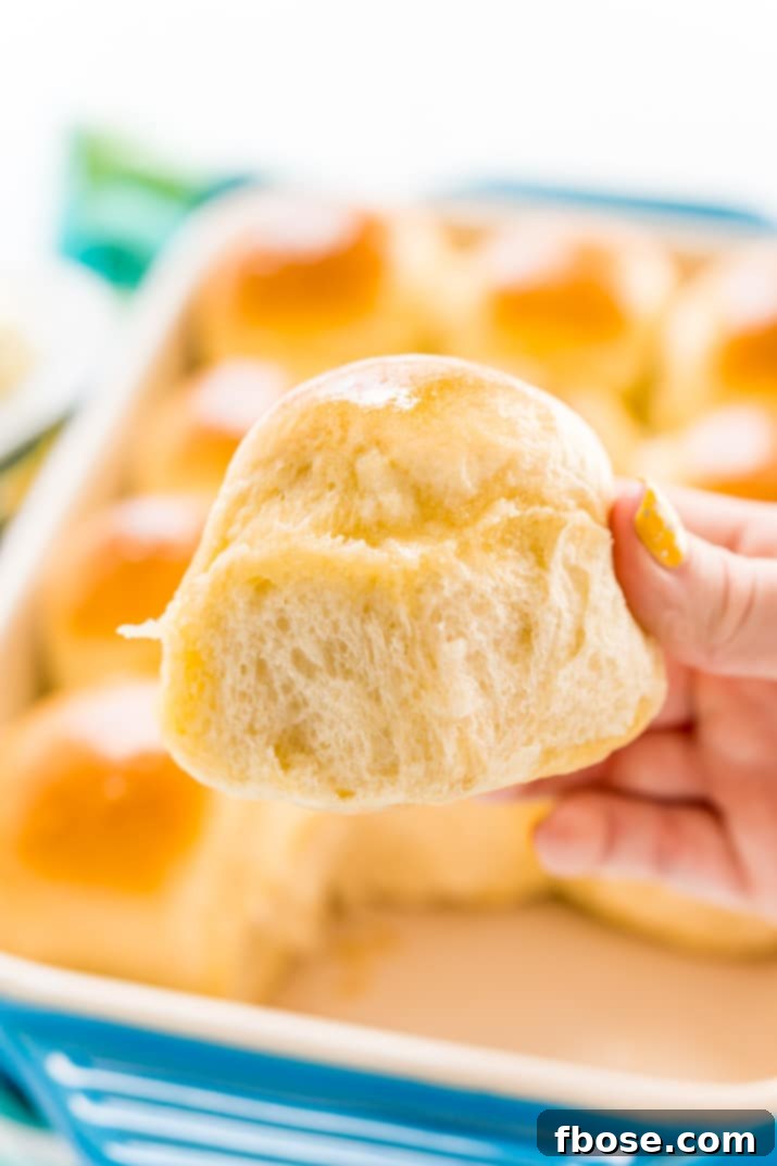 A woman's hand gently breaking apart a warm, freshly baked yeast roll, revealing its soft interior.