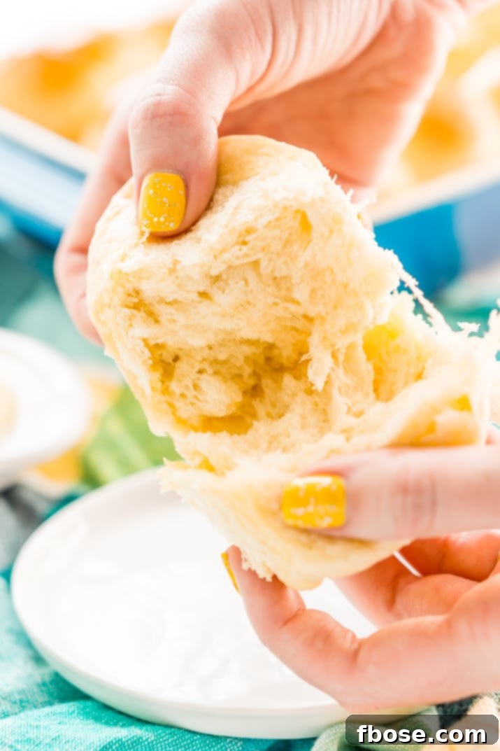 Close-up of hands pulling apart a warm, fluffy yeast roll, showing its soft, airy texture.