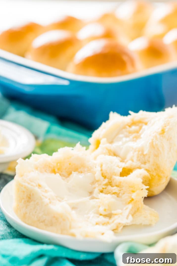 A small white plate holding two warm yeast rolls, one partially open, with a pat of butter melting on top.