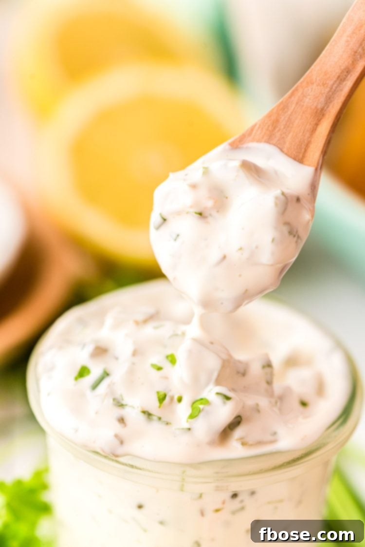 A spoonful of rich, creamy homemade tartar sauce being lifted from a glass jar, showing off its finely chopped ingredients and appealing texture.