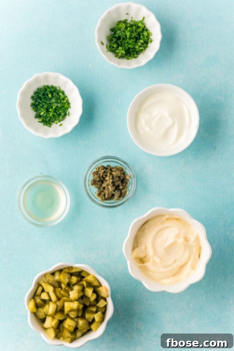 An inviting overhead photo of prepped ingredients for tartar sauce, including mayonnaise, Greek yogurt, chopped pickles, capers, parsley, and chives, neatly arranged for easy mixing.