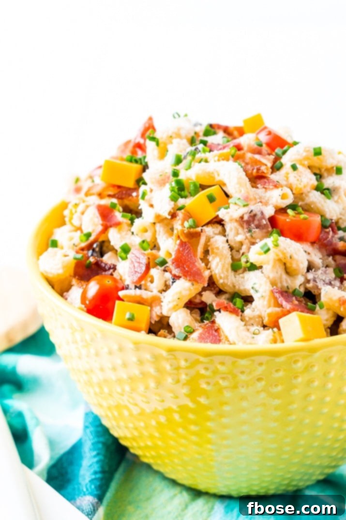 A serving spoon lifting a portion of Chicken Bacon Ranch Pasta Salad, showcasing the rich, creamy dressing clinging to every ingredient, ready to be served.