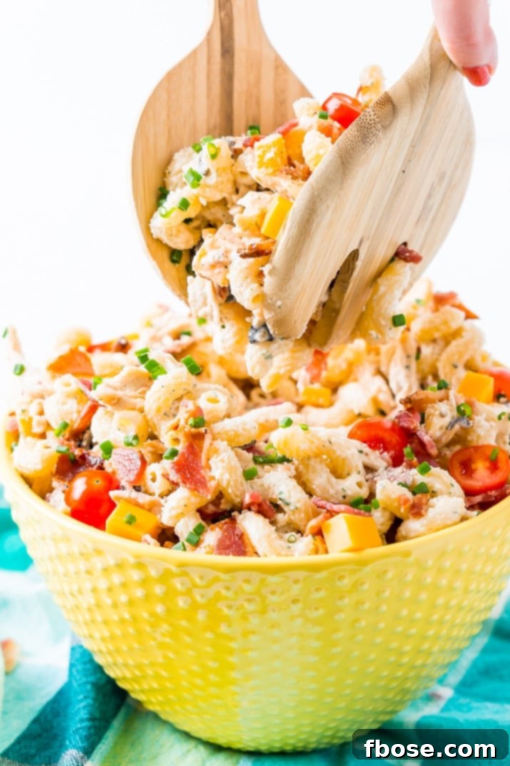 Overhead view of a large serving bowl filled with Chicken Bacon Ranch Pasta Salad, garnished with fresh chives, ready for a summer party.