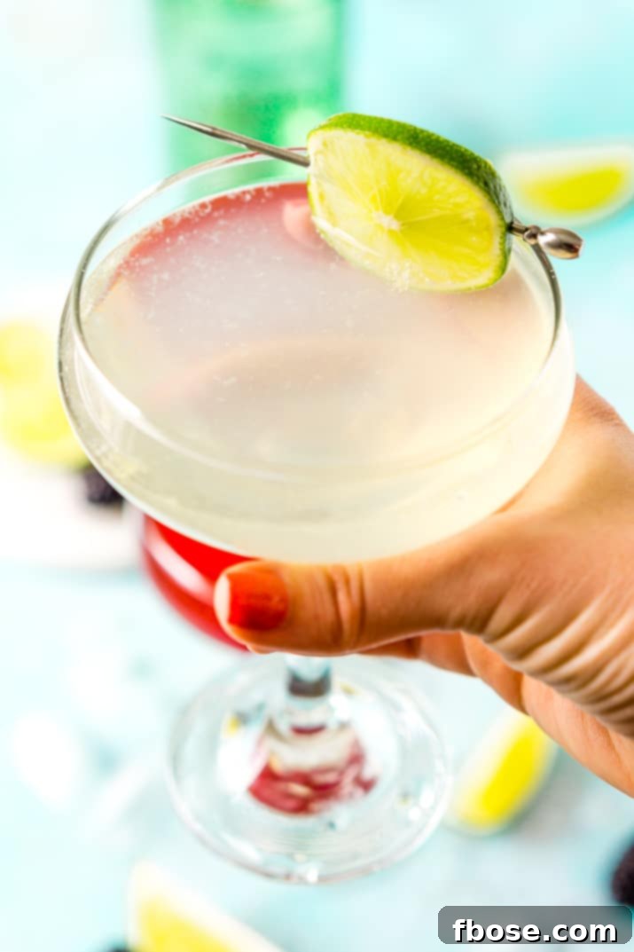 A classic Gimlet cocktail held in a woman's hand, against a blurred background, emphasizing its refreshing appeal.