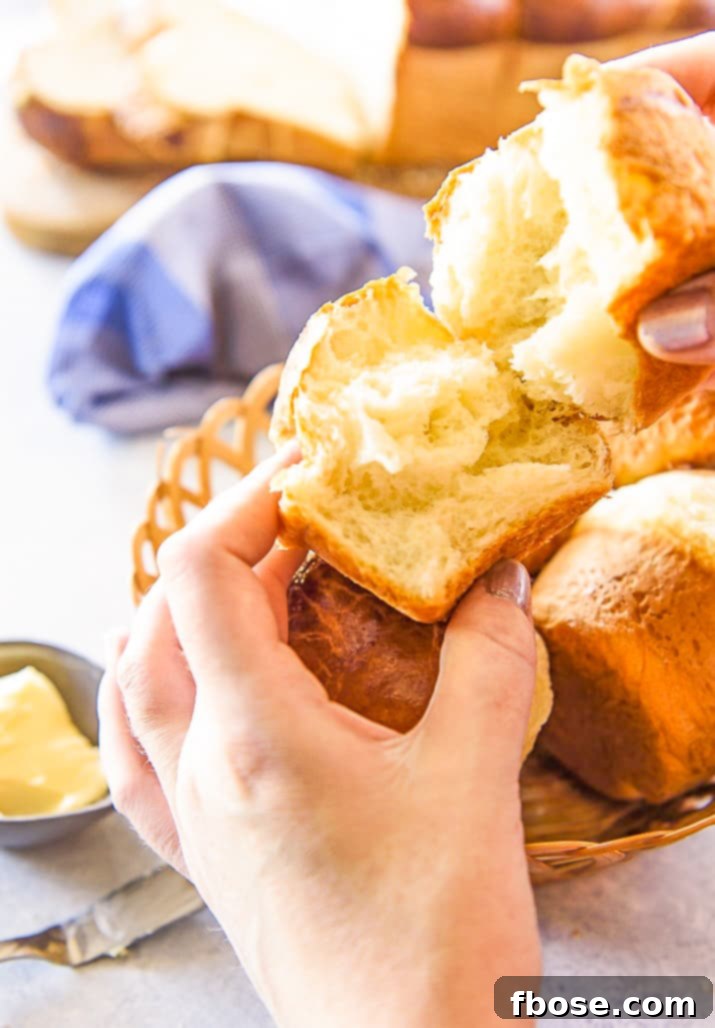 A woman's hands gently pulling apart a freshly baked brioche roll, revealing its soft, fluffy, and perfectly golden interior.