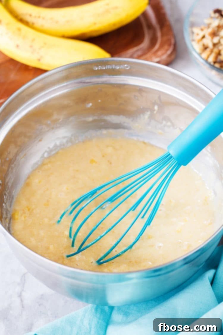Banana bread batter in a mixing bowl with a whisk, showing the creamy texture and flecks of mashed banana.