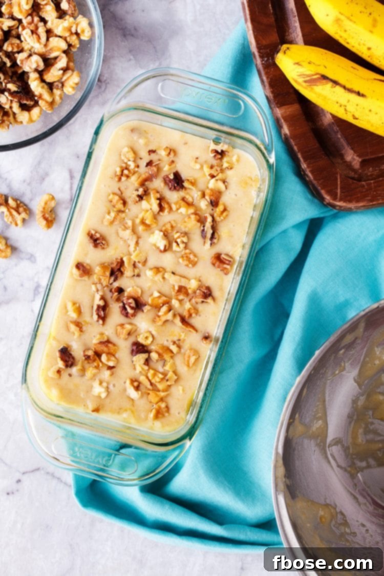 Banana bread batter in a loaf pan, topped with walnuts, ready for baking in the oven.