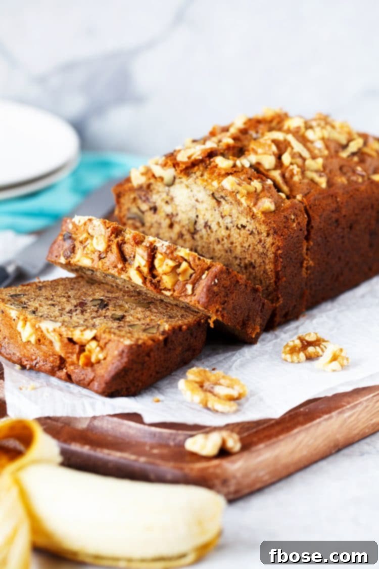A freshly baked loaf of banana bread, sliced on a wooden cutting board, revealing its moist interior and walnuts.