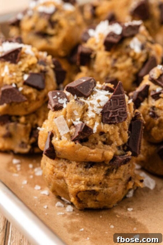 The Definitive Chocolate Chip Cookie 16 Stacked scoops of cookie dough on a parchment lined baking sheet.