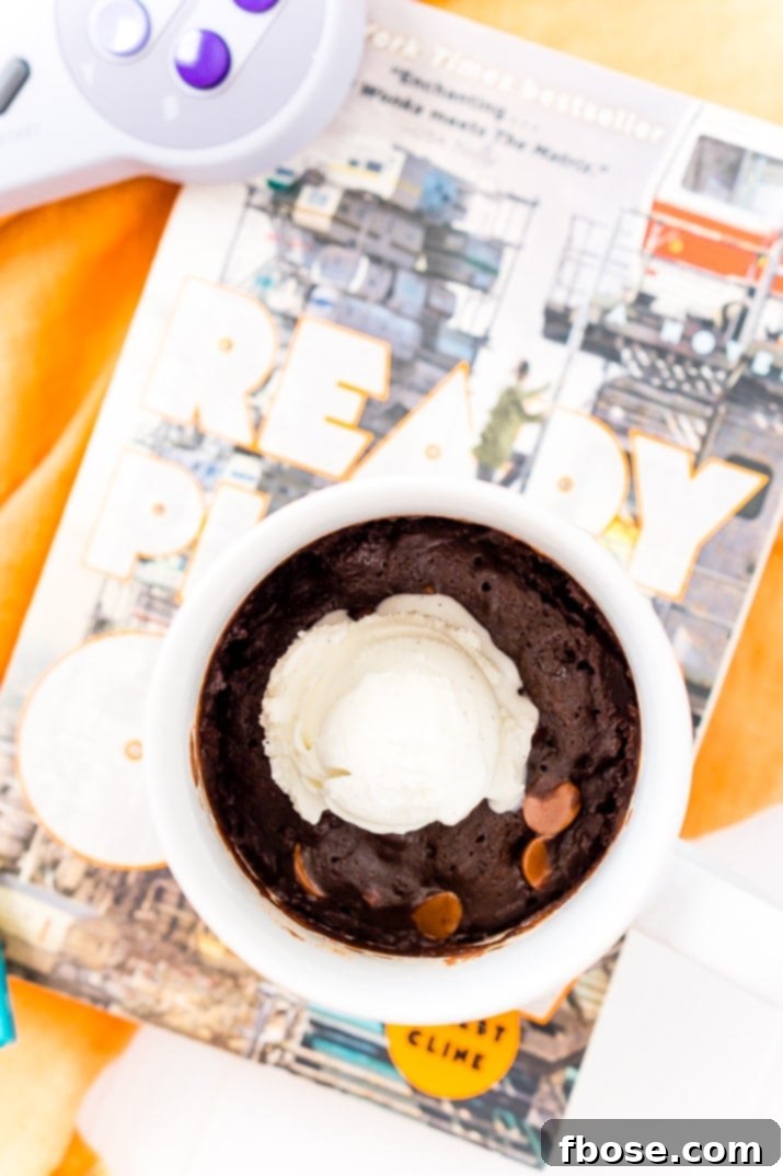 Microwave Brownie Mug Cake in a white mug, placed next to the 'Ready Player One' book, highlighting the recipe's literary inspiration.