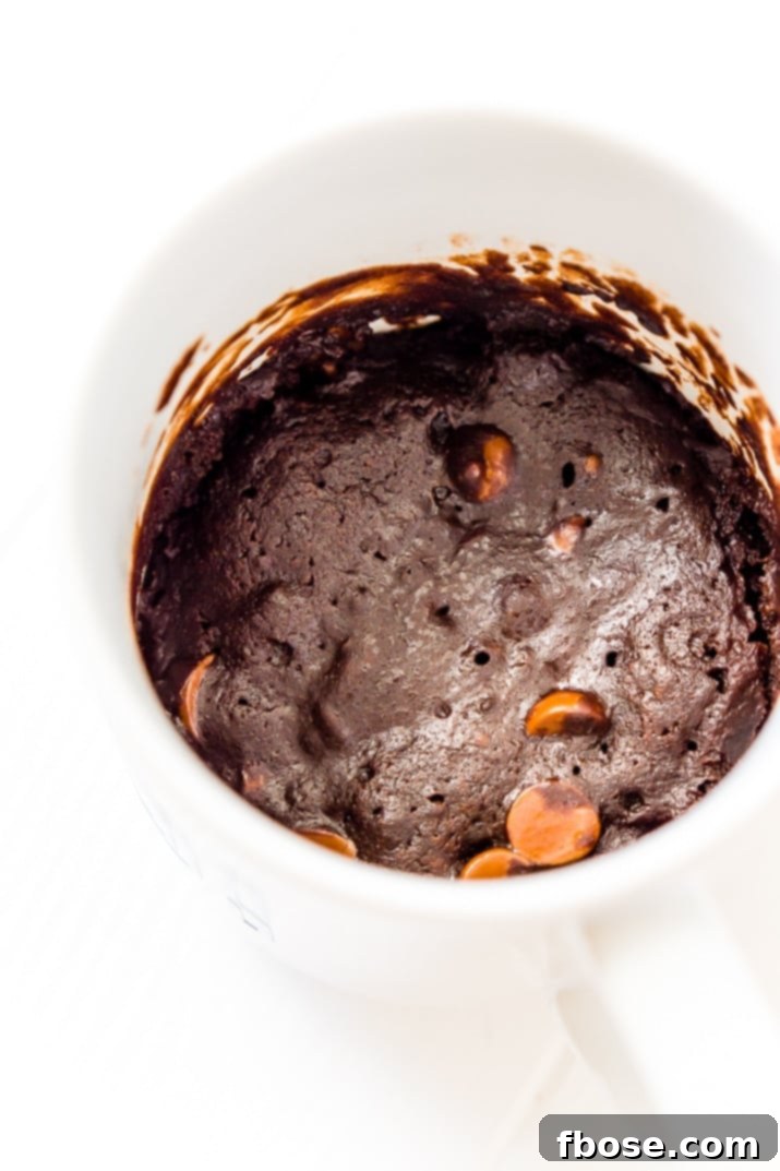 Close-up shot of a Microwave Brownie Mug Cake, showcasing its rich, dark chocolate color and moist texture, ready for a scoop of ice cream.