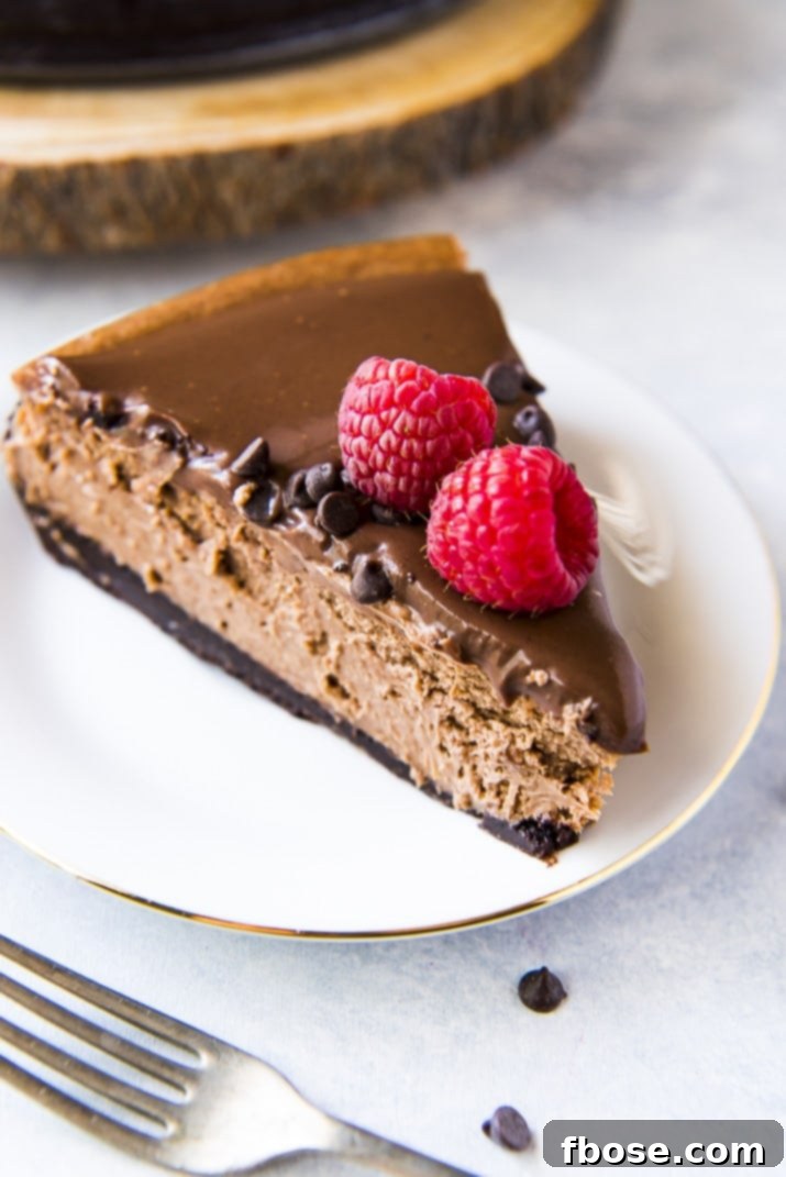 Slice of triple chocolate cheesecake garnished with fresh raspberries on a white plate