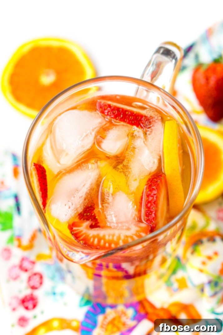 A close-up of a glass of White Wine Sangria with fresh strawberries, orange slices, and peaches, garnished with extra fruit for a perfect summer cocktail.