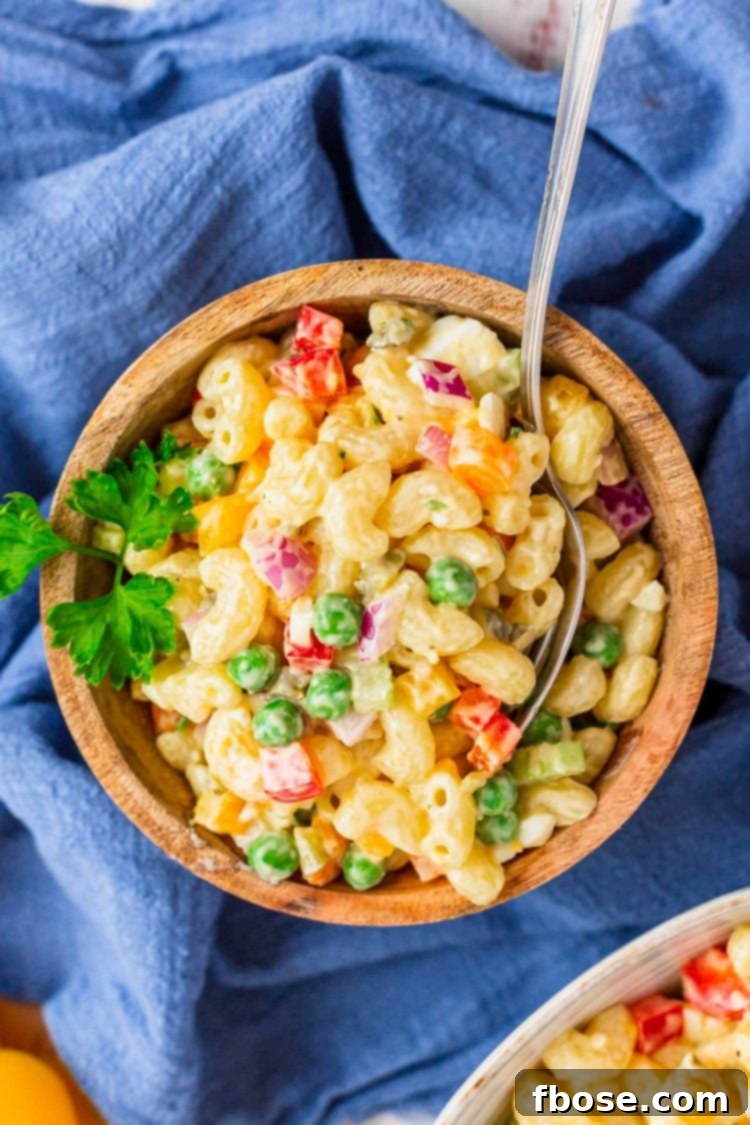 A wooden bowl generously filled with vibrant macaroni pasta salad, placed on a crisp blue and white checkered napkin. The salad is rich with elbow macaroni, colorful vegetables, and creamy dressing.