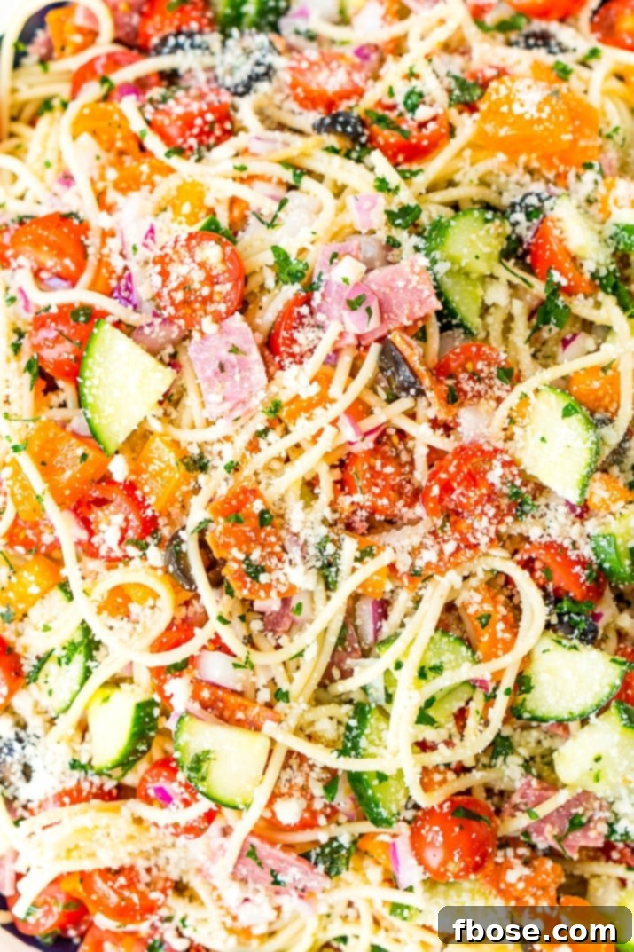 A vibrant and refreshing Spaghetti Salad, generously garnished with fresh parsley and grated Parmesan cheese, perfect for a summer gathering.