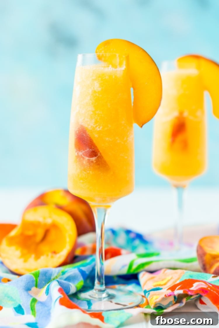 Two vibrant Peach Bellini Slushies in elegant glasses, garnished with fresh peach slices and mint sprigs, glistening with frost on a warm day.