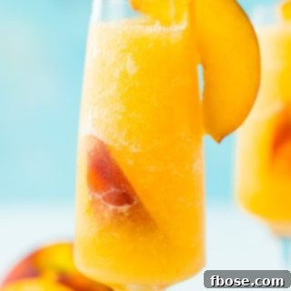 A vibrant Peach Bellini Slushie in a tall flute glass, garnished with fresh peach slices, ready for a refreshing sip.