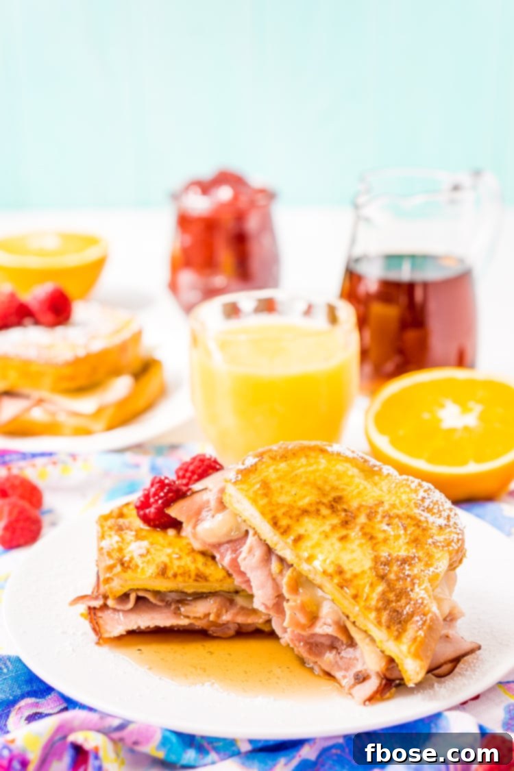 Two perfectly cooked Monte Cristo Sandwiches on a cutting board, dusted with powdered sugar and a small bowl of maple syrup, ready to be served.