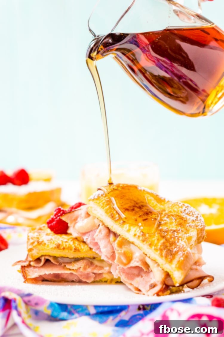 A freshly made Monte Cristo Sandwich, halved to reveal the delicious layers of ham and melted Swiss cheese, served on a plate with powdered sugar and maple syrup.