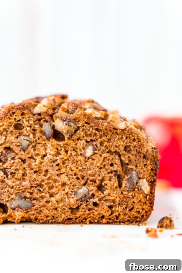 Close-up shot of a slice of Applesauce Bread, revealing its moist crumb, specks of spice, and chopped pecans. A perfect fall treat.