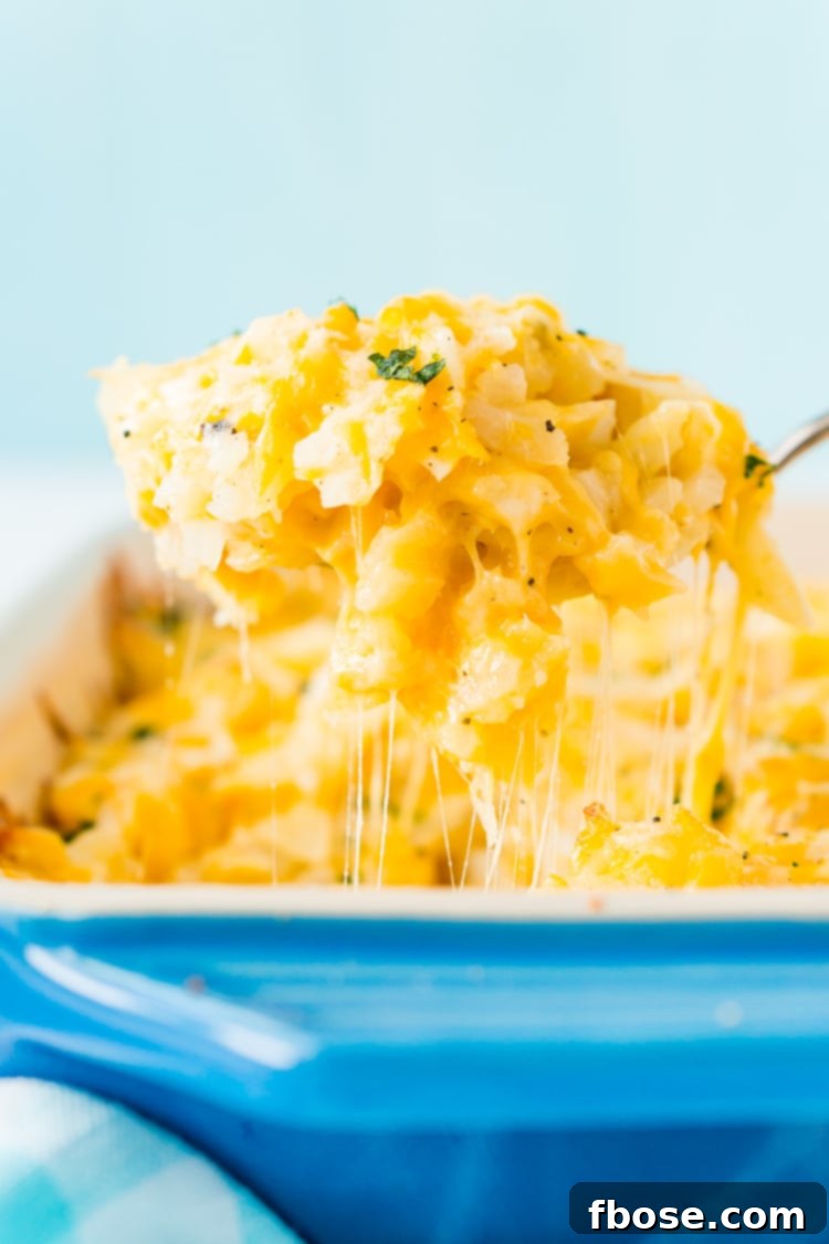 Serving spoon scooping a portion of creamy and cheesy Hashbrown Casserole, garnished with fresh herbs.
