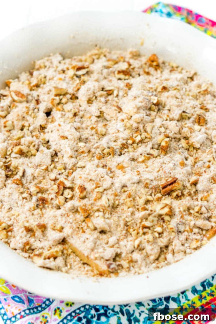 The crumbly pecan topping being sprinkled over the apple pie filling.