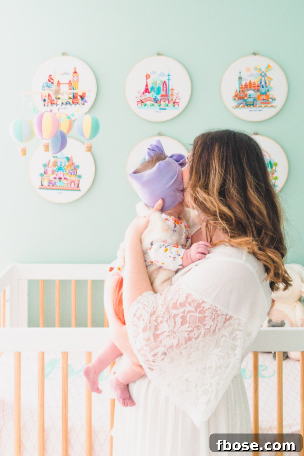 A loving woman holding her baby girl in front of a modern crib in a serene travel-themed nursery.