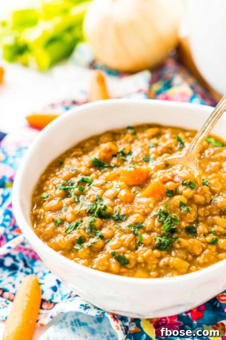 A close-up shot of a single lentil soup bowl on a dark background, garnished with a sprig of rosemary.