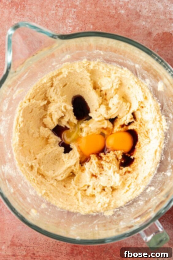 Egg being added to cookie dough being prepped in a bowl.