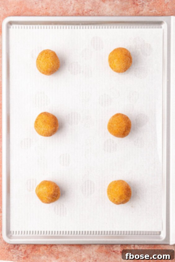Cookie dough balls on a parchment lined baking sheet.
