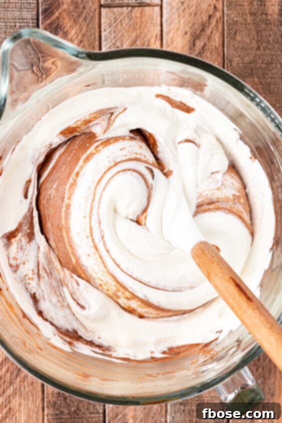 Whipped cream being poured into a chocolate pie mixture.