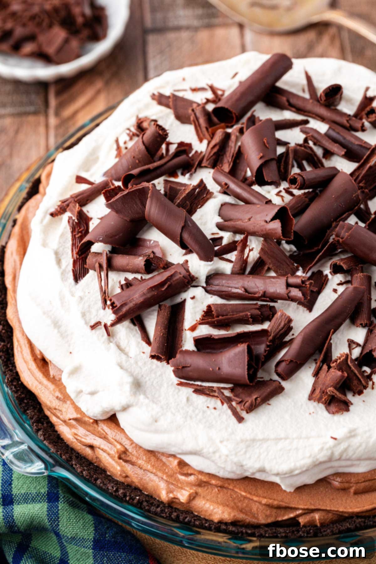 Close up of a French Silk Pie on a wooden table, showcasing its smooth chocolate filling and whipped cream.