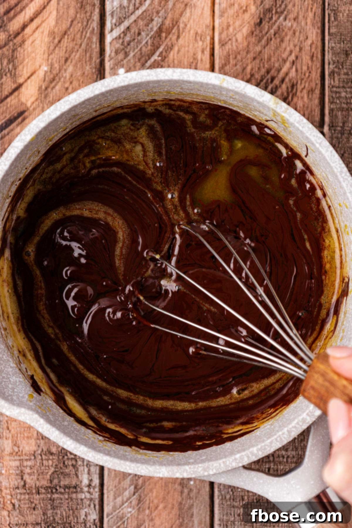 A whisk stirring chocolate and egg mixture in a pot to create the pie's filling.