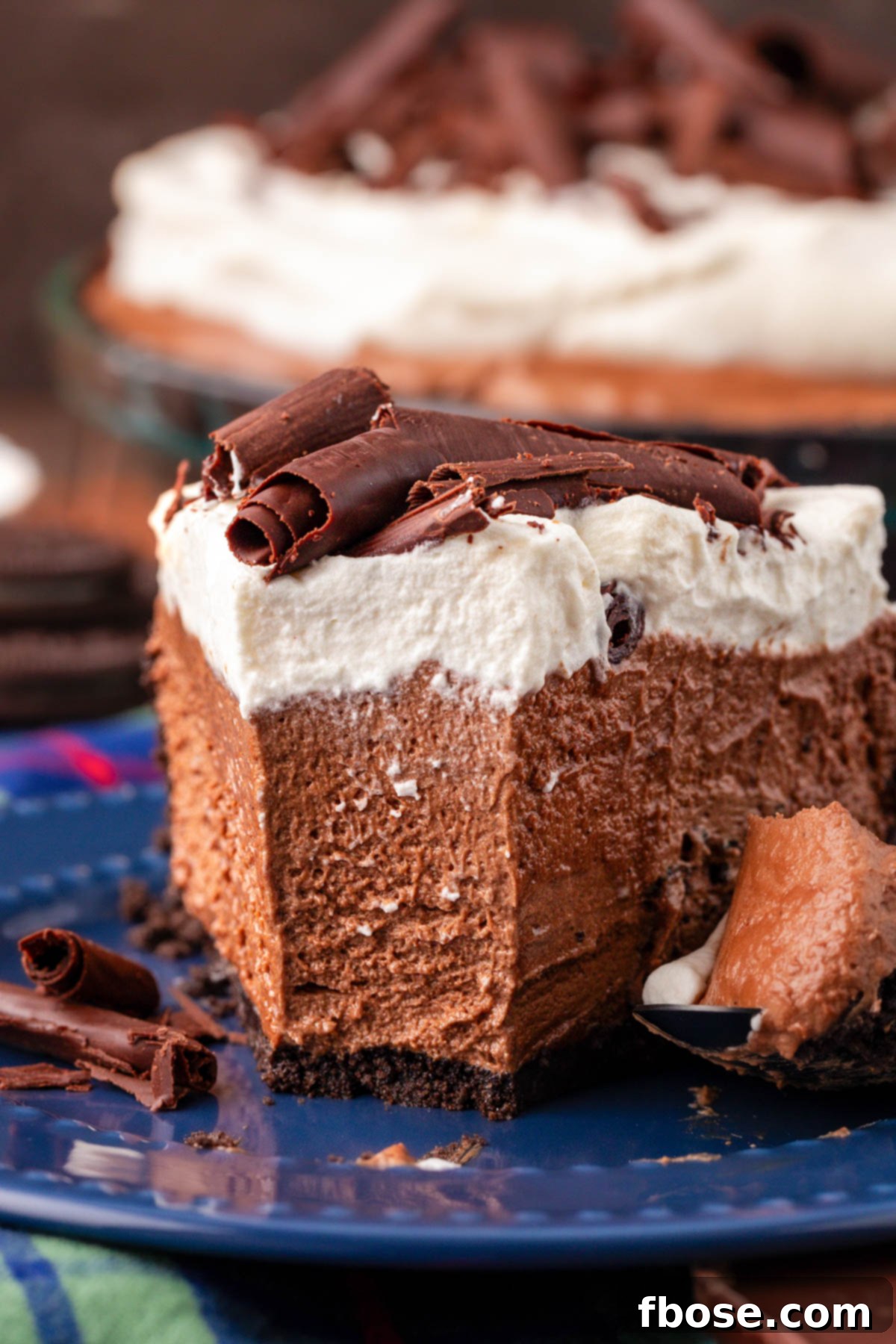 Close up of a slice of chocolate silk pie on a blue plate with a bite taken out, revealing the creamy layers.