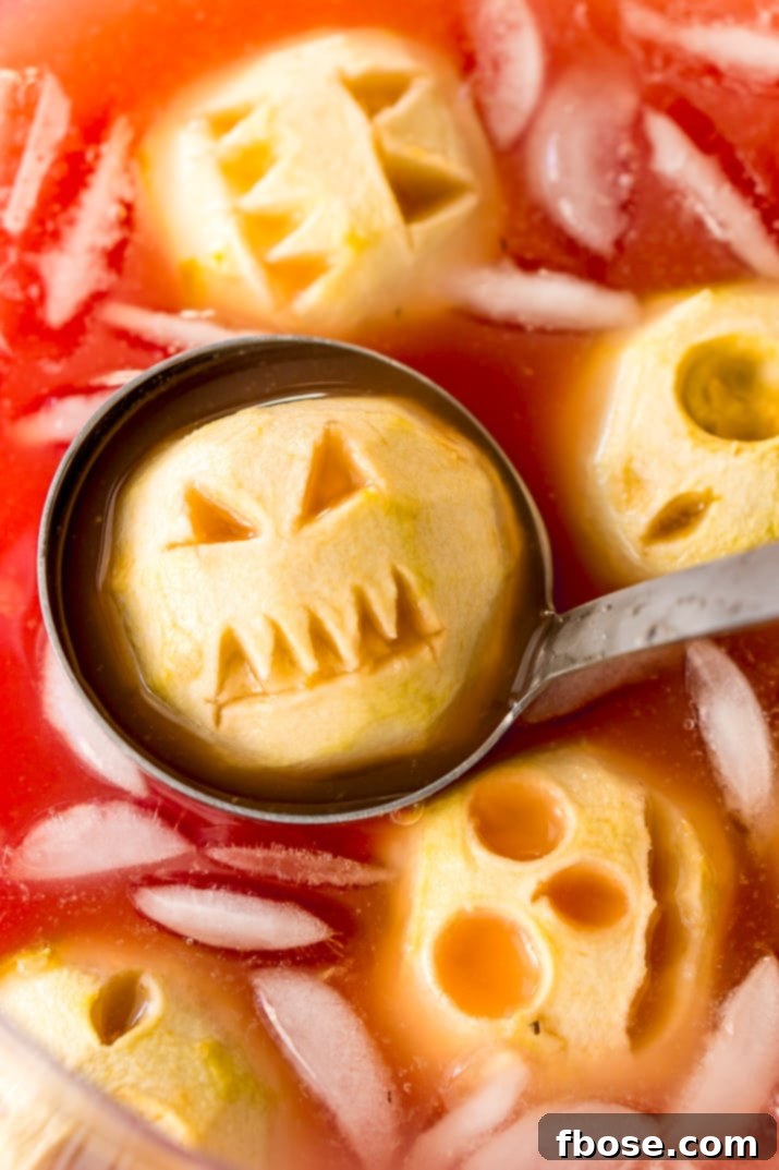 A large punch bowl filled with red Shrunken Head Party Punch, featuring eerie apple shrunken heads floating on top, with a ladle ready for serving.