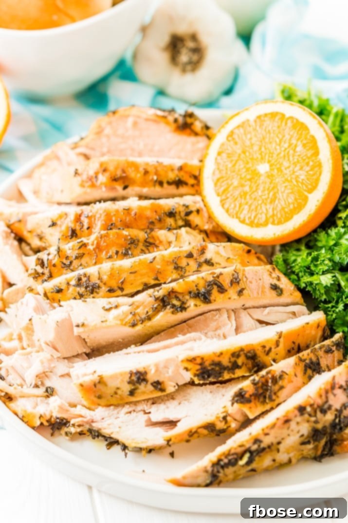 Sliced Turkey Breast with herbs on a white plate with half an orange, parsley, and garlic in the background.
