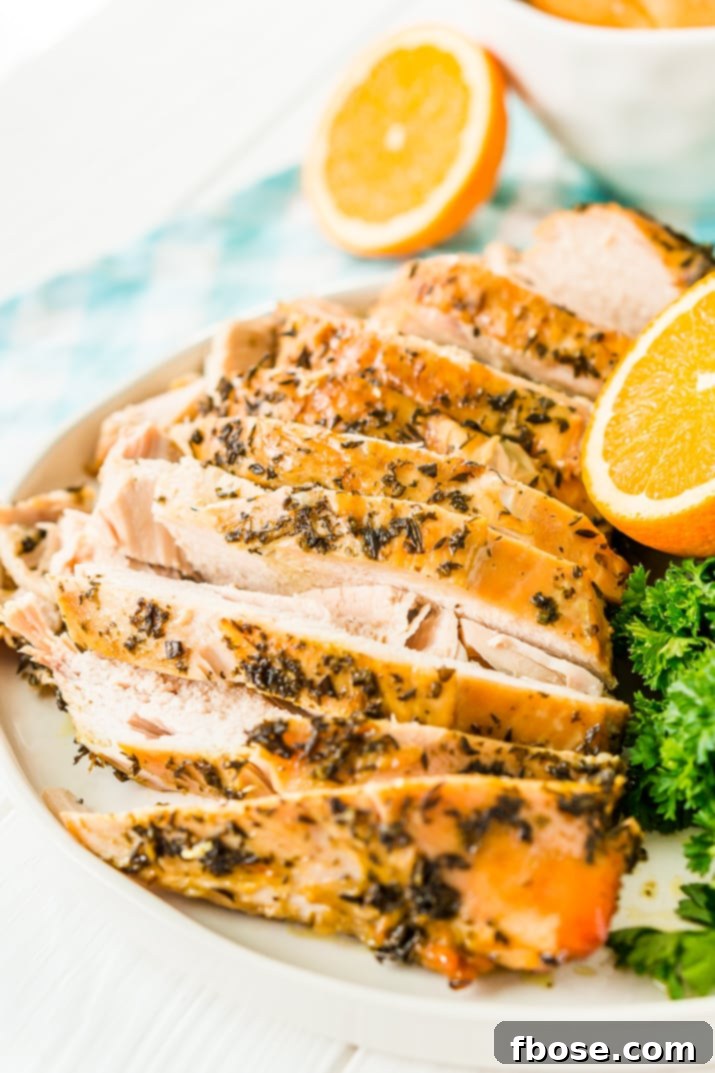Sliced Turkey Breast with herbs on a white plate with half an orange and parsley in the background.