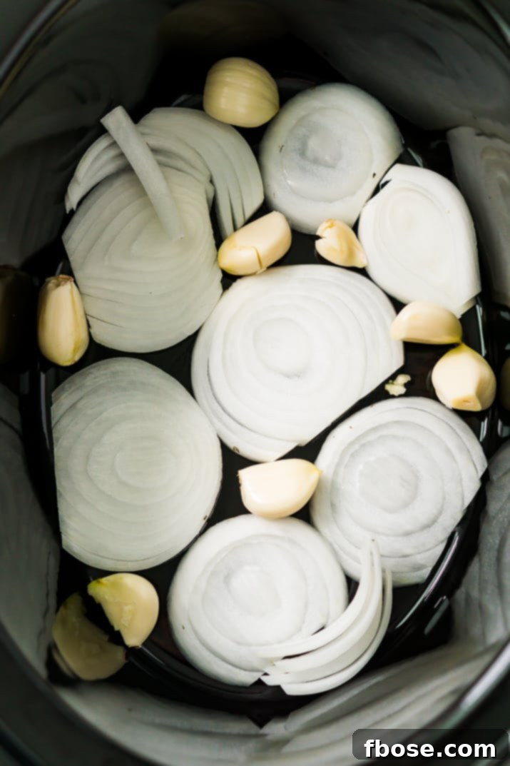 Onions and garlic in the bottom of a slow cooker.