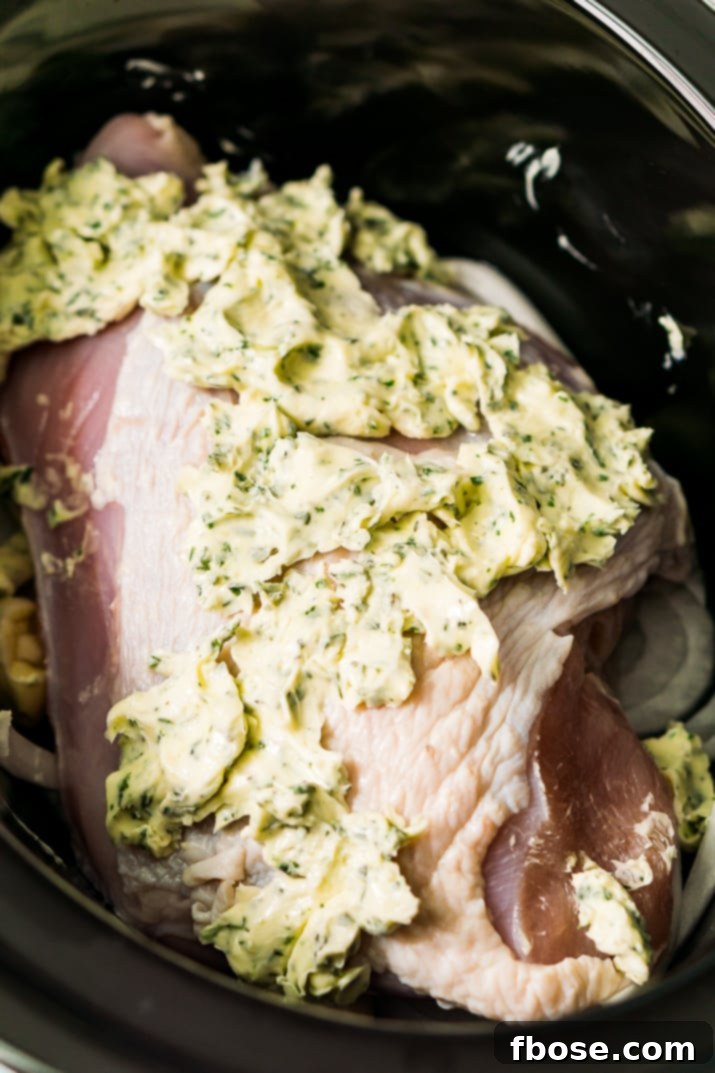 Turkey breast in a slow cooker covered in herb butter.