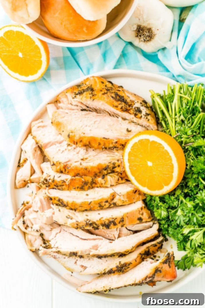 Overhead photo of a turkey breast covered in herbs and sliced on a plate with oranges and parsley.