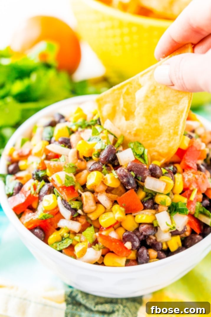 A vibrant bowl of Cowboy Caviar, bursting with colorful beans, corn, peppers, and tomatoes, sits ready for dipping. It's a Mexican-inspired dip or topping loaded with fresh ingredients and zesty spices, perfect for game day snacks, barbecues, and taco nights.