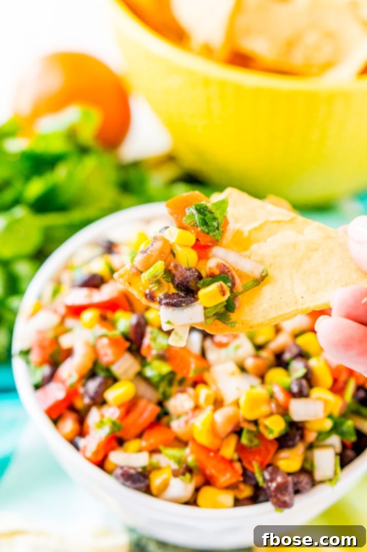 A woman's hand proudly holds a tortilla chip generously loaded with a scoop of colorful Cowboy Caviar, showcasing the perfect consistency and the inviting freshness of the dip.