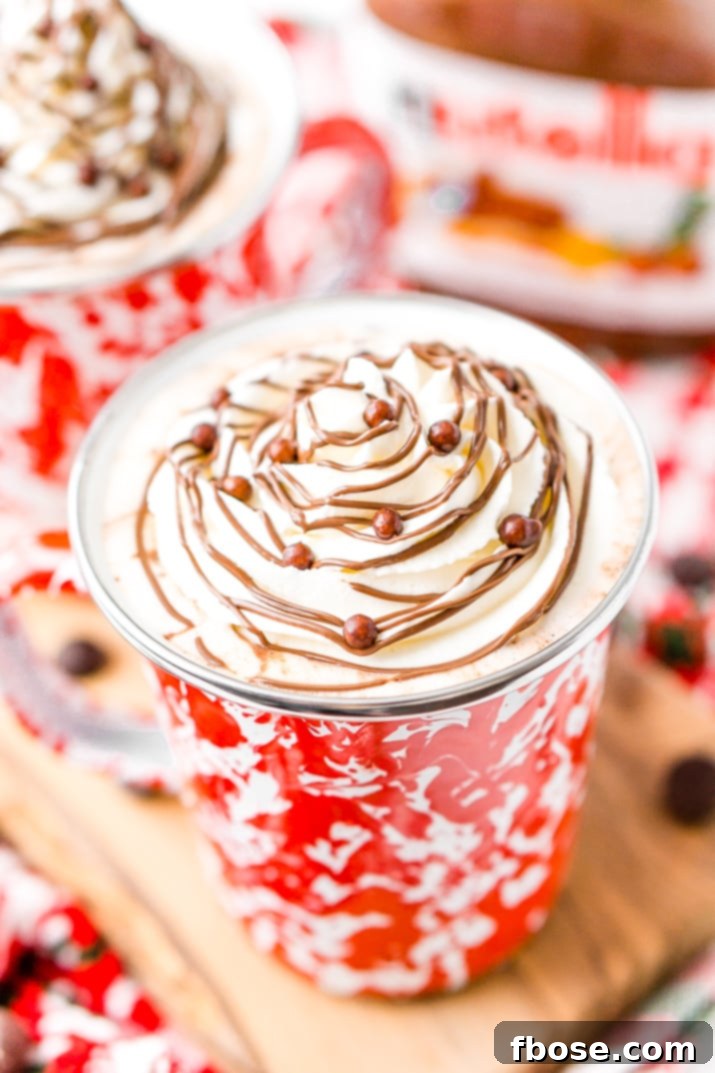 A hand holding a mug of Nutella Hot Chocolate, showing the steam rising and promising warmth.