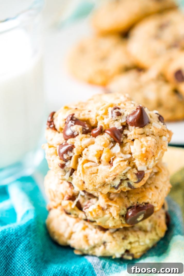 Three Lactation Cookies stacked on top of each other on turquoise napkin with milk and plate of cookies in the background.