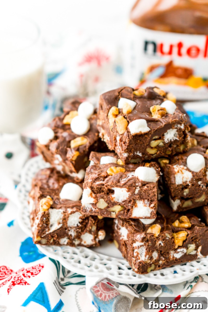 Nutella Rocky Road Fudge squares arranged on a white plate, with a tub of Nutella in the background, highlighting the key ingredient.